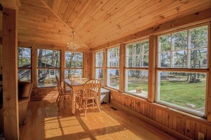 Ein Holzblockbau-Innenraum mit Esstisch, Stühlen, großen Fenstern und einer Chandelier.