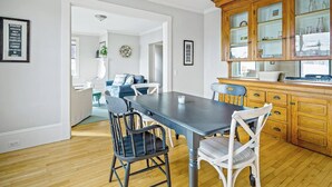 A dining area with a table and chairs, a kitchen with wooden cabinets, and a living room with a sofa and a plant. - Harborwalk (Camden)