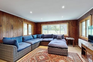 Ein Zimmer mit einer großen Eckcouch, einem kleinen Tisch, einem Fernseher und großen Fenstern.