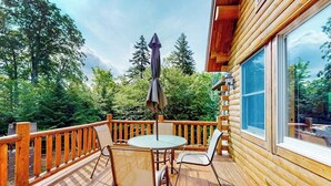 A wooden deck with a table and chairs, surrounded by a railing, overlooking a forested area. - Tranquil Haven Secluded Waterfront House With Sauna, Dock, Kayaks, Canoe, gym (Greenville)