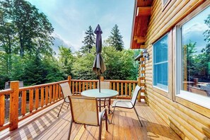 Eine Holzterrasse mit Tisch und Stühlen, umgeben von einem Geländer, mit Blick auf ein bewaldetes Gebiet.