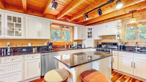 A spacious kitchen with wooden beams, white cabinetry, a granite countertop, and two stools. - Tranquil Haven Secluded Waterfront House With Sauna, Dock, Kayaks, Canoe, gym (Greenville)