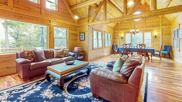A log cabin interior with a living area, dining table, and large windows. - Tranquil Haven Secluded Waterfront House With Sauna, Dock, Kayaks, Canoe, gym (Greenville)