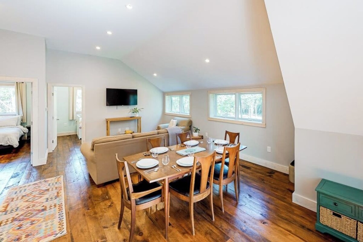 A dining area with a wooden table set for four, a sofa, and a TV mounted on the wall.
