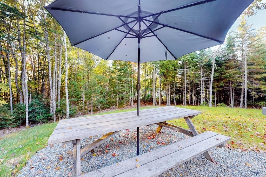A wooden picnic table with an umbrella in a forested area.