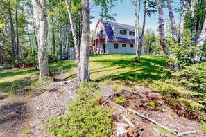 A house surrounded by a forest with a grassy yard and a metal roof. - Partridge Cove (Ellsworth)