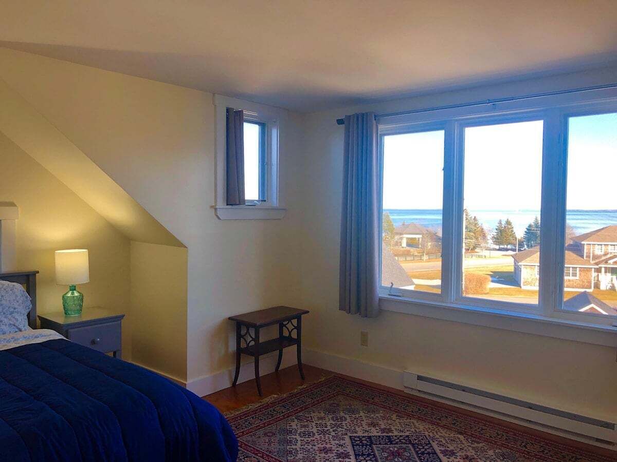 A bedroom with a bed, a nightstand, a table, a window with a view of the outside, and a ceiling with a skylight.