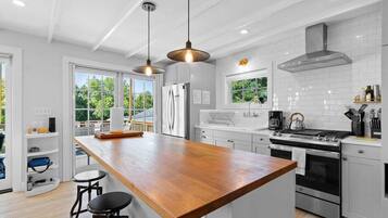 A modern kitchen with a wooden island, stainless steel appliances, pendant lighting, and large windows.