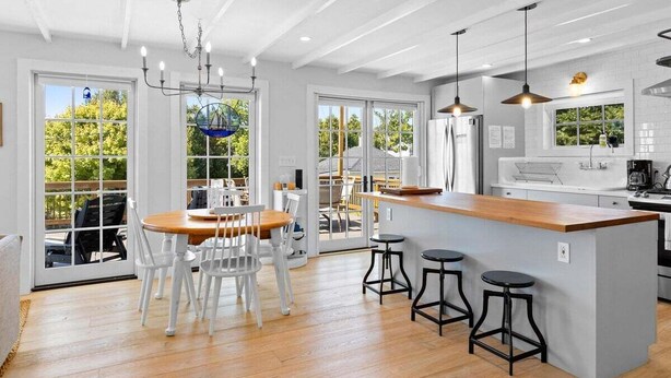 Una cucina moderna con isola in legno, sedie bianche e illuminazione a sospensione.