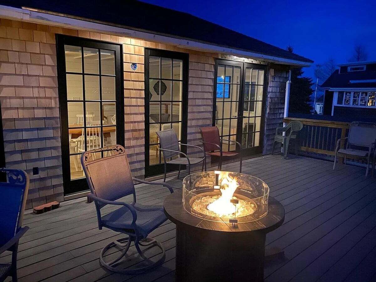 Una terraza con una fogata, sillas y un edificio con ventanas amplias.
