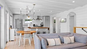 Una cucina moderna con mobili bianchi, un'area pranzo con tavolo in legno e sedie bianche, e un divano grigio con cuscini.