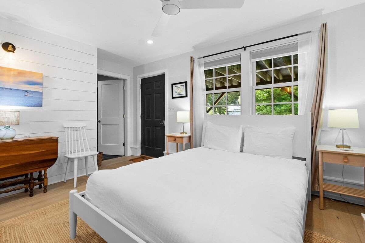 A bedroom with a bed, bedside tables, a dresser, a window with curtains, and a painting on the wall.