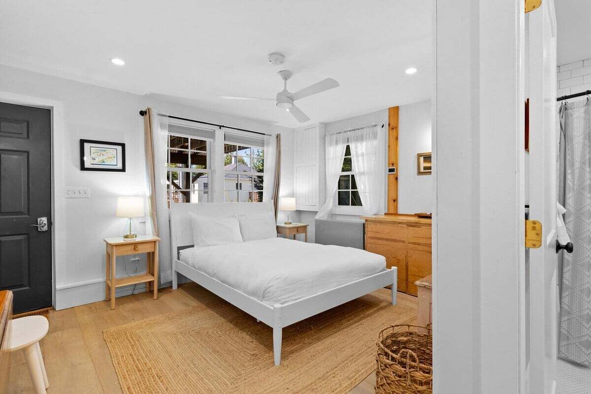 Quarto com cama, mesas de cabeceira, ventilador de teto e janela com cortinas.