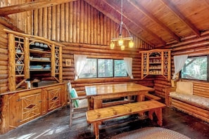 A log cabin interior with a wooden dining table, benches, and shelves with glassware. - Stunning log Cabin With Fireplace & Nature Views - Near Shopping & Dining (Boothbay Harbor)
