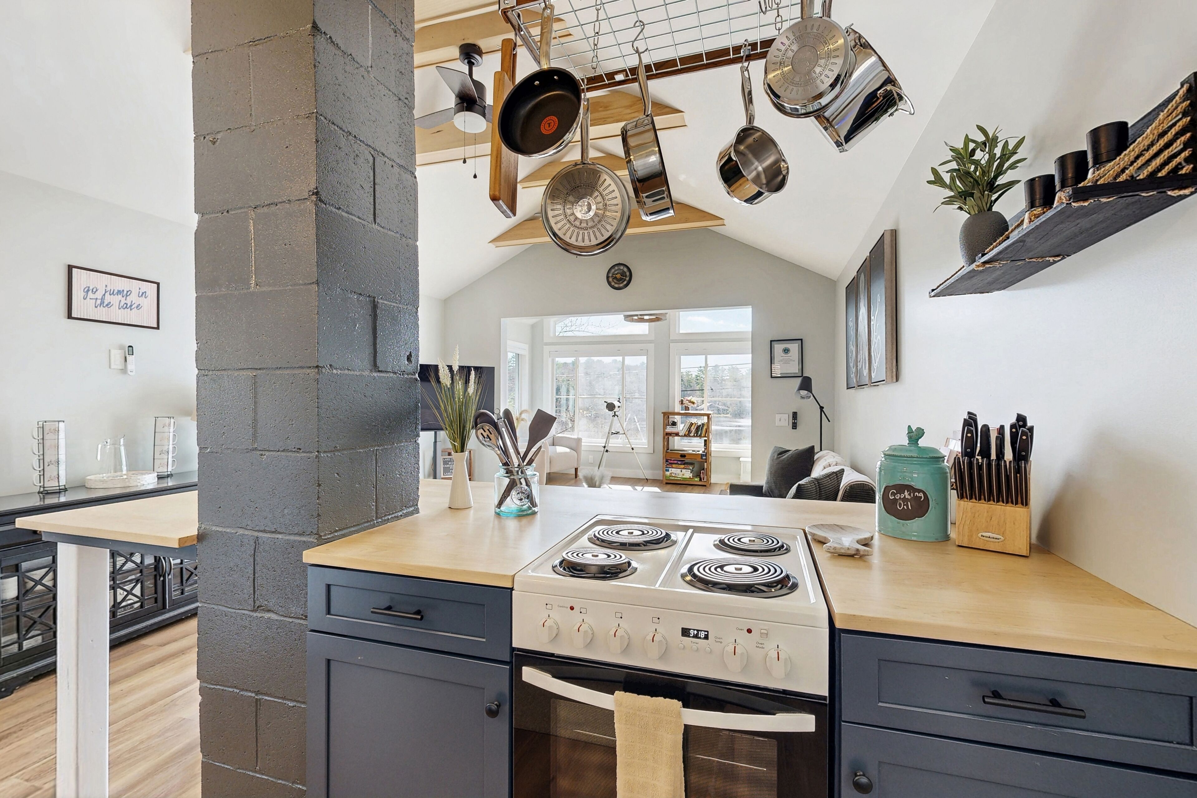 A kitchen with a stove, oven, hanging pots, and a coffee maker on the counter.