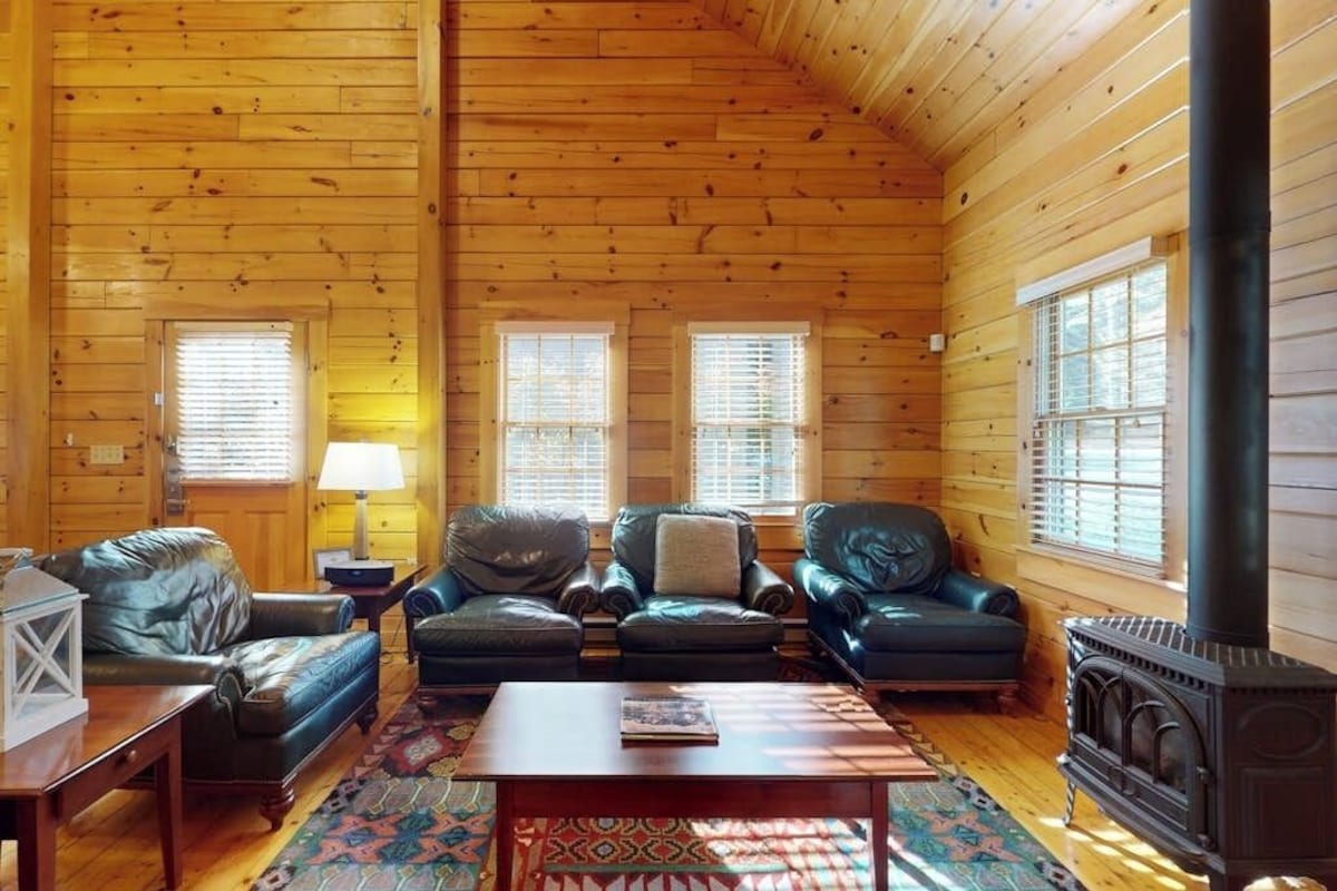 Ein Holzblockhaus-Interieur mit Kamin, Ledersofas und einem gemusterten Teppich.