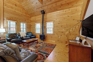 A log cabin interior with a fireplace, leather sofas, and a wooden staircase. - Point Lookout East (Lincolnville)