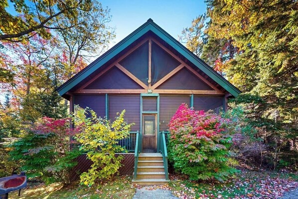A cabin with a steeply pitched roof, a front door, and a small set of stairs leading to the entrance. - Point Lookout East (Lincolnville)
