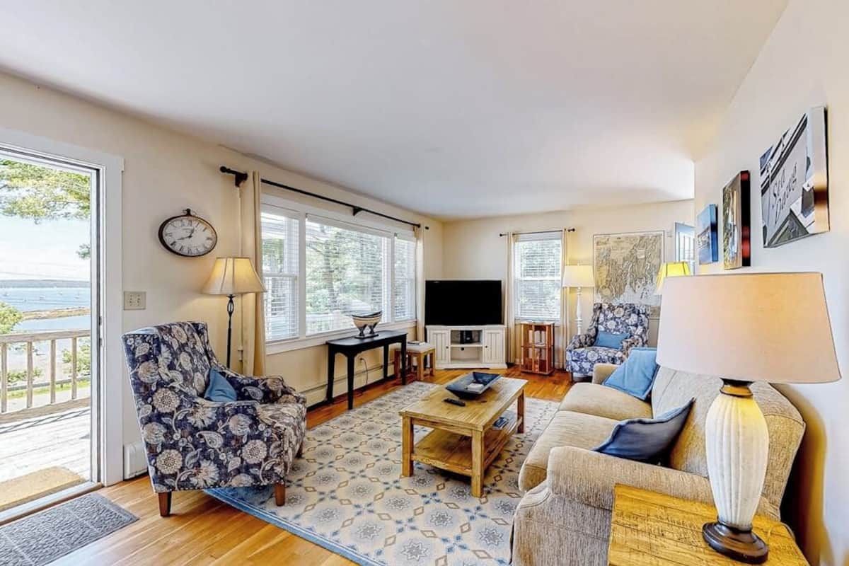 Una sala de estar con sofá, sillón, mesa de centro, televisor y ventana con vistas.