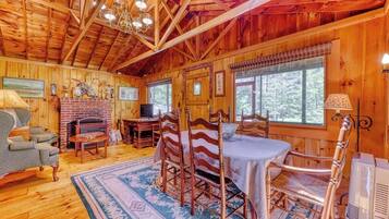 A wooden cabin interior with a dining area, fireplace, and large windows.