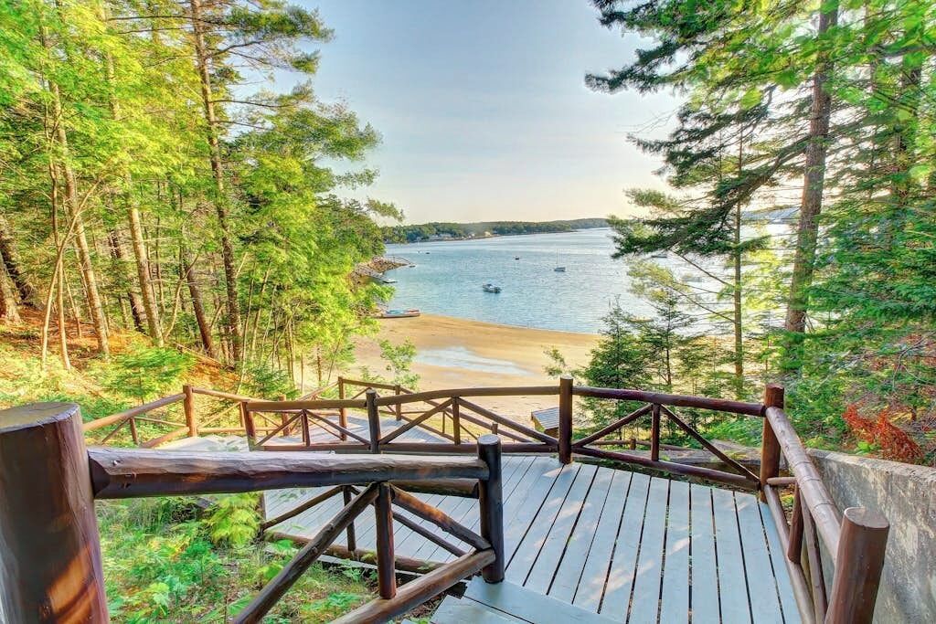A wooden deck with a railing overlooking a beach and a forested area.