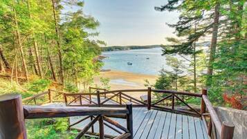 A wooden deck with a railing overlooking a beach and a forested area.