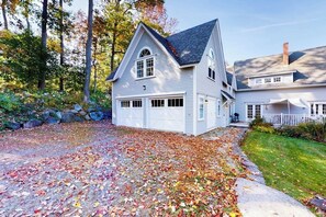 A two-story house with a garage, surrounded by trees and a stone wall. - Harbor House (Camden)