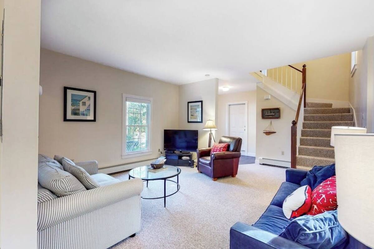 A living room with a sofa, armchair, coffee table, TV, and a staircase.