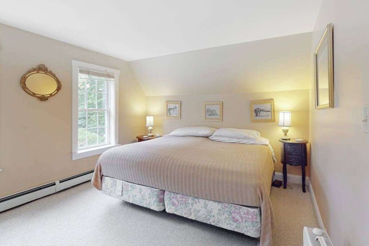 A bedroom with a bed, a window, a mirror, and wall-mounted lamps.