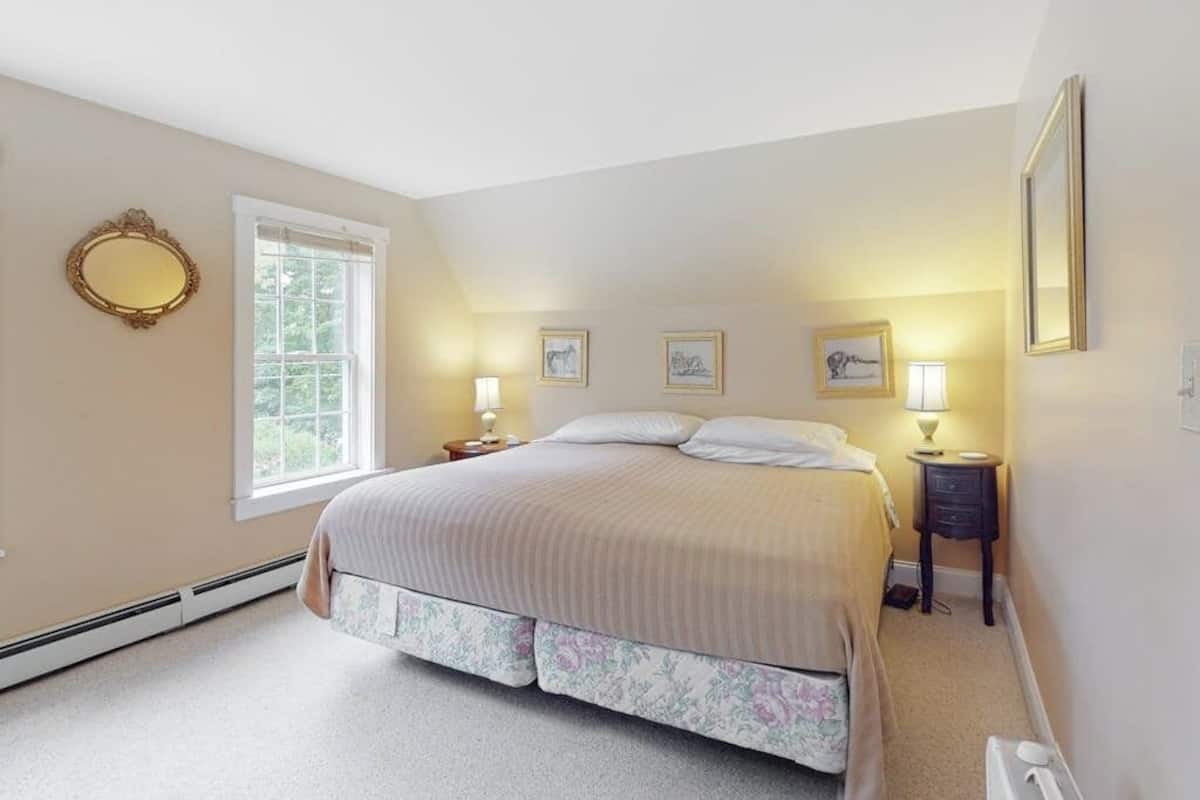 A bedroom with a bed, a window, a mirror, and wall-mounted lamps.