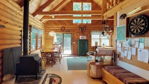 A log cabin interior with a fireplace, wooden furniture, a dartboard, and a bulletin board. - Dog-friendly Lakefront Log Cabin With Peaceful Atmosphere, Dock & Boat Launch (Rockwood)