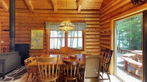 A log cabin interior with a dining table, chairs, a map, a fireplace, and a view of the outdoors. - Dog-friendly Lakefront Log Cabin With Peaceful Atmosphere, Dock & Boat Launch (Rockwood)