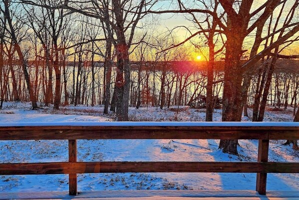 Un banc en bois dans un paysage enneigé, avec des arbres sans feuilles et un coucher de soleil en arrière-plan.