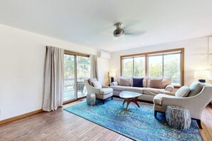 Ein geräumiges Wohnzimmer mit großem Fenster, Deckenventilator und blauem Teppich.
