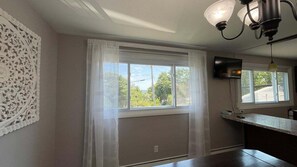 A room with a large window, a decorative wall panel, a flat-screen TV, and a kitchen counter. - Penobscot View, 4 Bedroom Home in Rockland Maine (Rockland)
