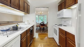 A kitchen with wooden cabinets, a white microwave, a stove, and a dishwasher. - Birch Tree Lane (Bar Harbor)