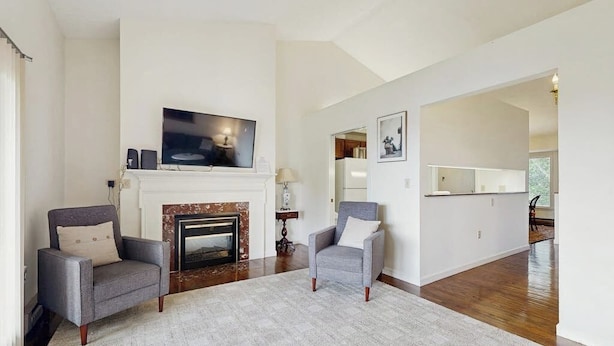 A living room with a fireplace, two armchairs, a television, and a hallway leading to another room. - Birch Tree Lane (Bar Harbor)