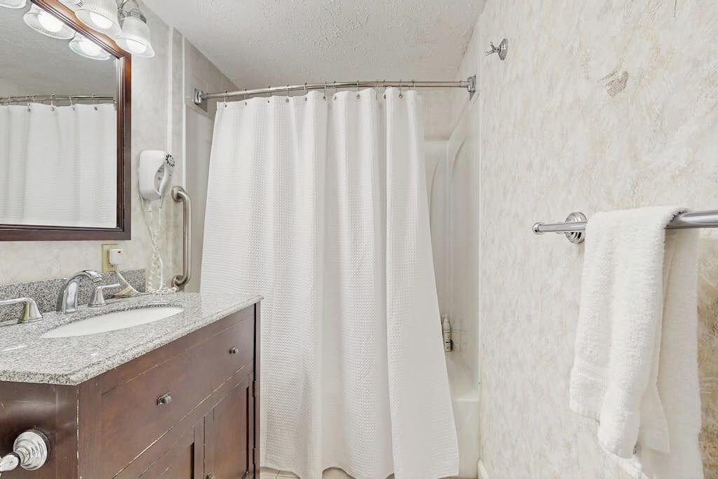 A bathroom with a sink, mirror, towel rack, and shower curtain.