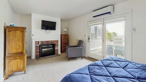 A bedroom with a bed, a TV, a fireplace, a wardrobe, and a balcony. - Birch Tree Lane (Bar Harbor)