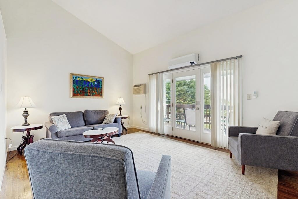 A living room with a sofa, armchairs, a coffee table, a painting, and a sliding glass door leading to an outdoor area.