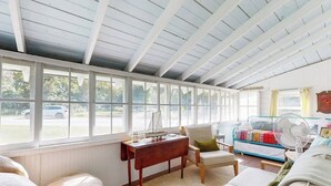 A room with a high ceiling, large windows, a wooden desk, a sofa, and a bed with a colorful blanket. - Charming Boothbay Harbor Cottage With Partial AC, Full Kitchen, and sun Room (Boothbay Harbor)