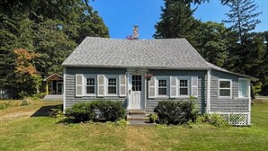 A single-story house with a gray shingled roof, white trim, and a front door. - Charming Boothbay Harbor Cottage With Partial AC, Full Kitchen, and sun Room (Boothbay Harbor)