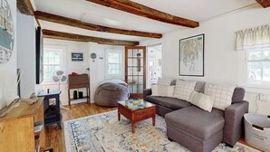 A cozy living room with a sofa, a coffee table, a wooden desk, and a large window. - Charming Boothbay Harbor Cottage With Partial AC, Full Kitchen, and sun Room (Boothbay Harbor)