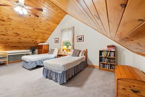 A cozy attic bedroom with two beds, a desk, a fan, and a bookshelf. - Riverfront Home w/ Deck, Amazing Views & Firepit - Near the Best of Maine (Stockton Springs)