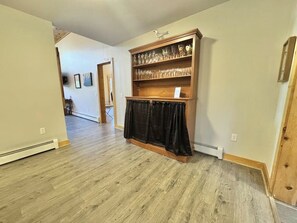 A room with wooden flooring, a built-in shelf with glassware, and a black curtain. - Riverfront Home w/ Deck, Amazing Views & Firepit - Near the Best of Maine (Stockton Springs)