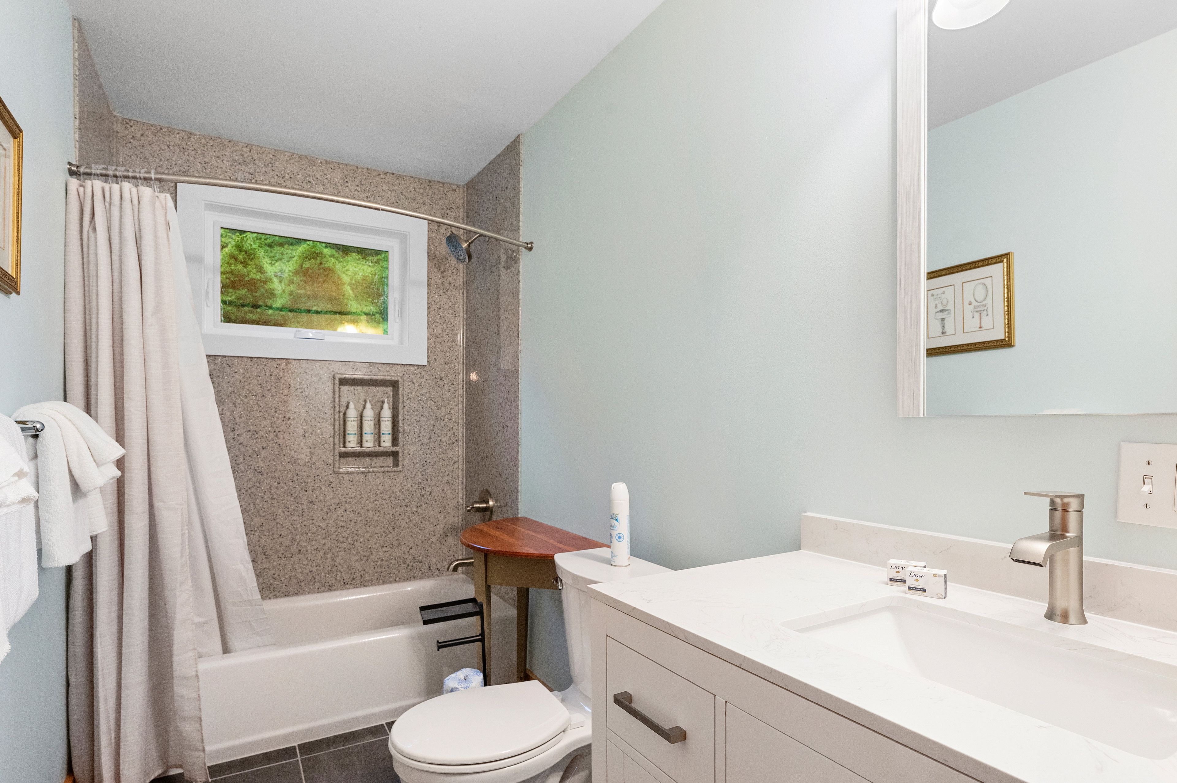 Ein Badezimmer mit Badewanne, Toilette, Waschbecken und einem Fenster mit Blick auf Bäume.