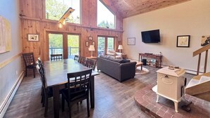 A spacious room with a wooden ceiling, a dining table with chairs, a sofa, a television, and a fireplace. - Riverfront Home w/ Deck, Amazing Views & Firepit - Near the Best of Maine (Stockton Springs)