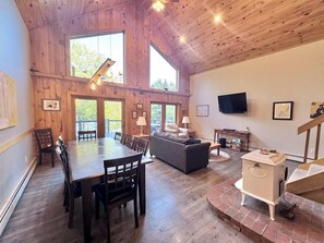 A spacious room with a wooden ceiling, a dining table with chairs, a sofa, a television, and a fireplace. - Riverfront Home w/ Deck, Amazing Views & Firepit - Near the Best of Maine (Stockton Springs)