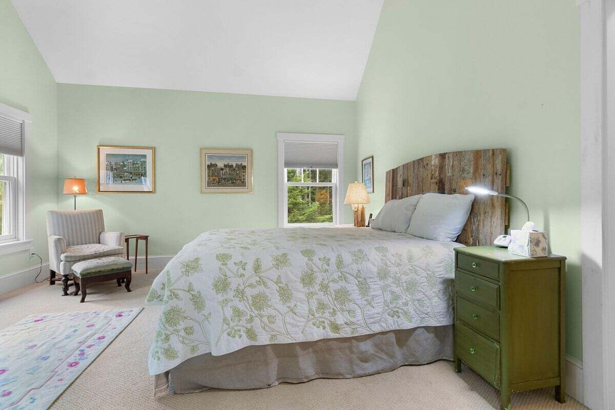 A bedroom with a bed, a chair, a nightstand, and two framed pictures on the wall.