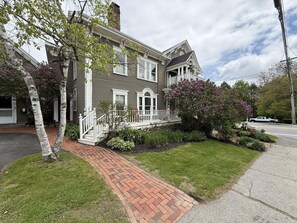 A two-story house with a brick pathway leading to the front door, surrounded by well-maintained grass and shrubs. - Commanders Cabin, Quaint apt Steps to Downtown (Camden)